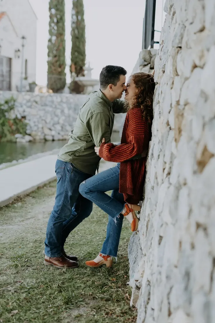 Engagement session, couple kissing against a stone wall
