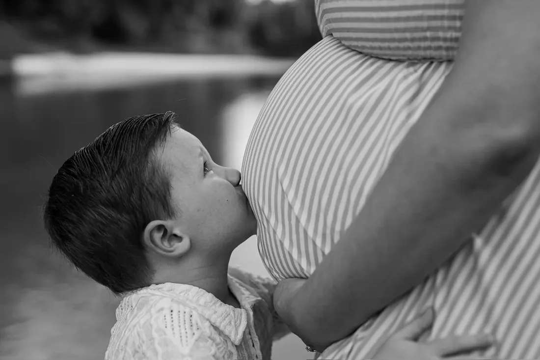 Toddler kissing his pregnant mother's belly, black and white
